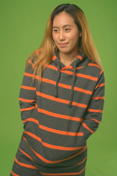 Jong aziatisch vrouw dragen hoodie tegen groen achtergrond — Stockfoto