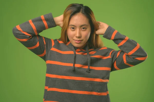 Jong aziatisch vrouw dragen hoodie tegen groen achtergrond — Stockfoto
