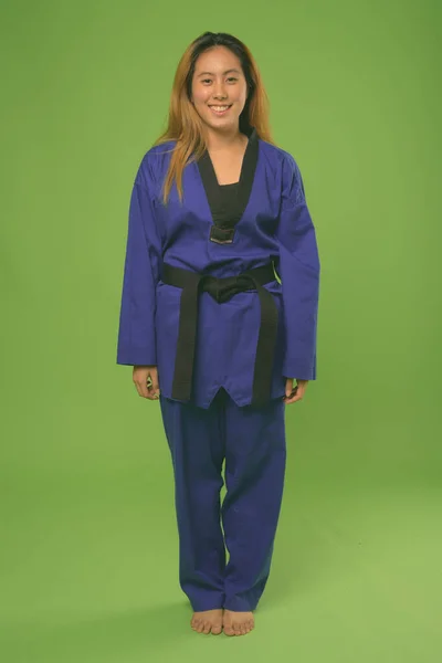 Mladý asijské žena nošení modrý karate gi proti zelenému pozadí — Stock fotografie