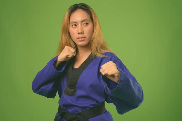 Jovem mulher asiática vestindo azul karatê Gi contra fundo verde — Fotografia de Stock