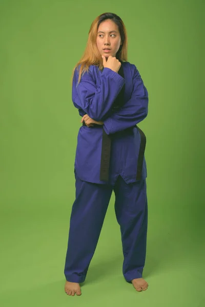 Young Asian woman wearing blue karate Gi against green background — Stock Photo, Image