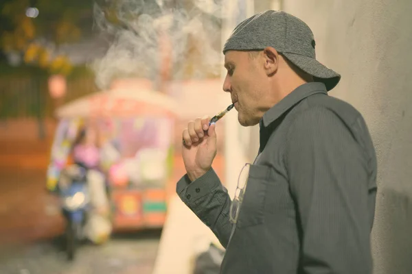 Mature man smoking electronic cigarette in the streets at night — Stock Photo, Image