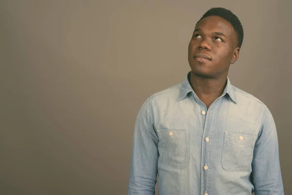 Mladý africký muž v džínové košili na šedém pozadí — Stock fotografie