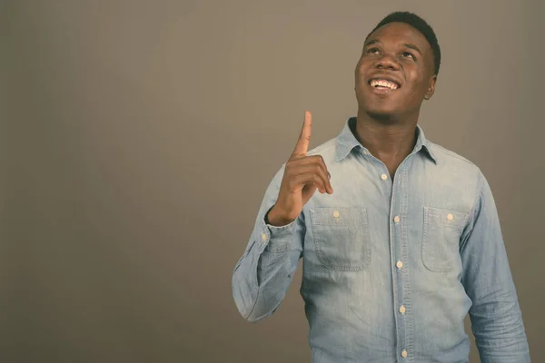Ung afrikansk man bär jeansskjorta mot grå bakgrund — Stockfoto