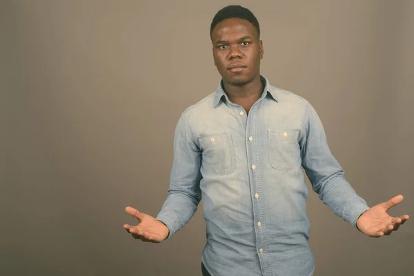 Young African man wearing denim shirt against gray background — Stock Photo, Image