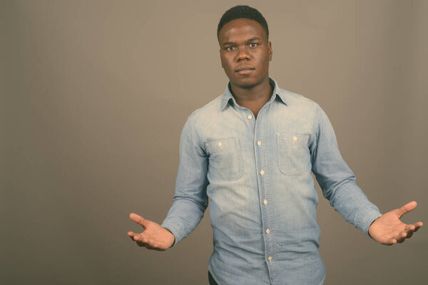 Studio shot of young African man wearing denim shirt against gray background