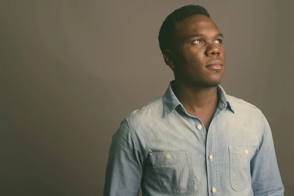 Молодий африканський чоловік одягнений у джинсову сорочку на сірому фоні. — стокове фото