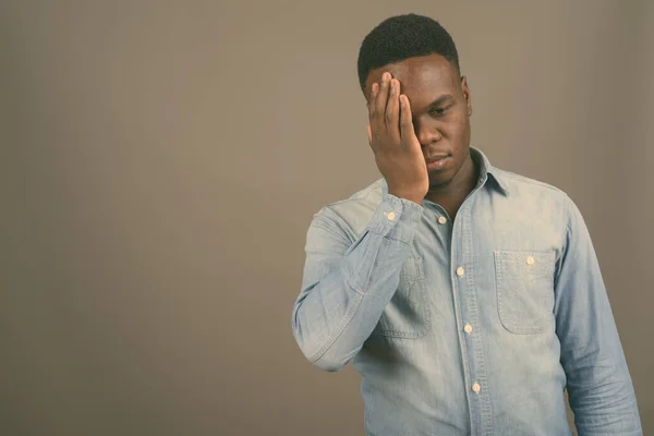 Jonge Afrikaanse man draagt denim shirt tegen grijze achtergrond — Stockfoto