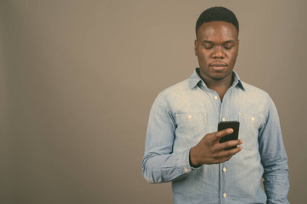 Studio shot of young African man using mobile phone against gray background