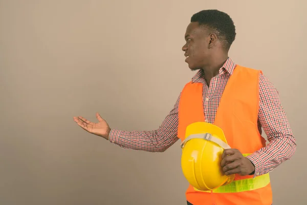 Jovem Africano trabalhador da construção mostrando algo contra fundo branco — Fotografia de Stock