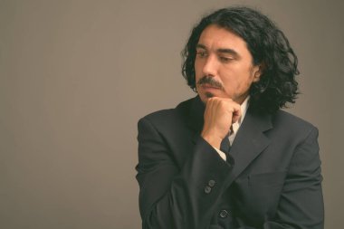 Bıyıklı yakışıklı iş adamı gri arka planda takım elbise giyiyor.