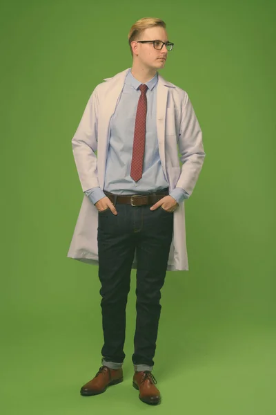 Young handsome man doctor with blond hair against green background — Stock Photo, Image