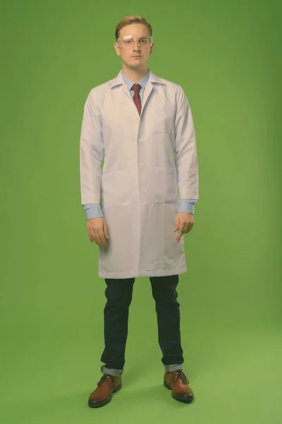 Pemuda tampan dokter dengan rambut pirang mengenakan kacamata pelindung terhadap latar belakang hijau — Stok Foto