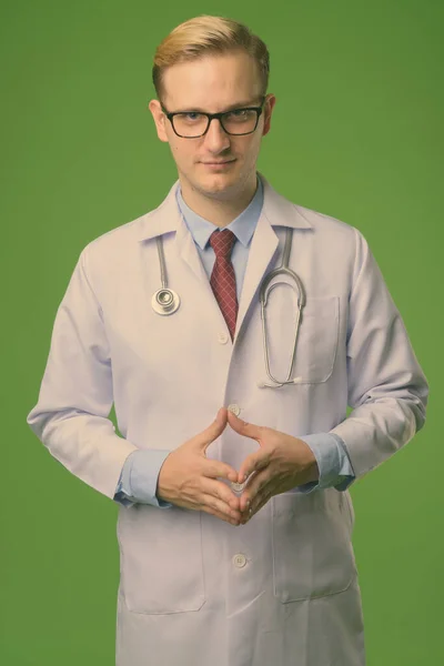 Joven hombre guapo médico con el pelo rubio sobre fondo verde — Foto de Stock