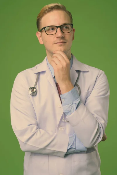 Joven hombre guapo médico con el pelo rubio sobre fondo verde — Foto de Stock