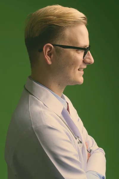 Junger schöner Mann Arzt mit blonden Haaren vor grünem Hintergrund — Stockfoto