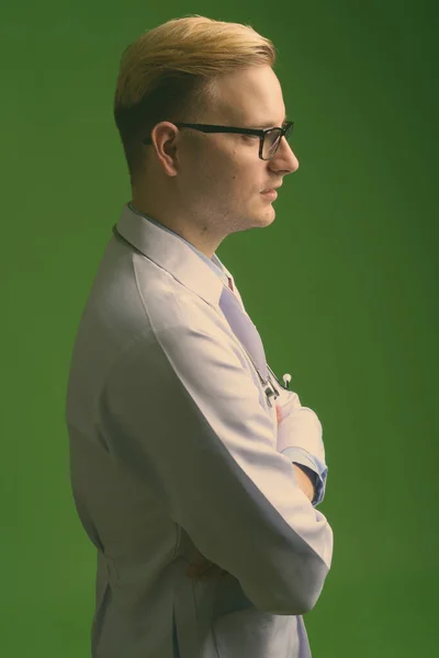 Mladý pohledný muž lékař s blond vlasy proti zelenému pozadí — Stock fotografie