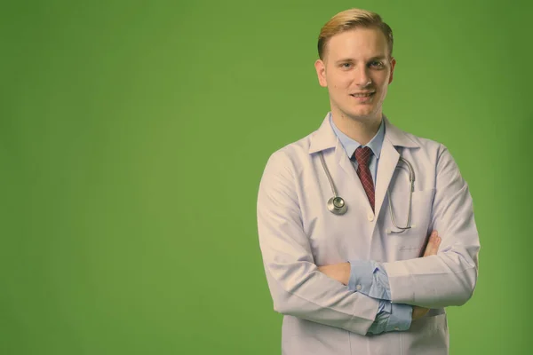 Νέος όμορφος άντρας γιατρός με ξανθά μαλλιά σε πράσινο φόντο — Φωτογραφία Αρχείου