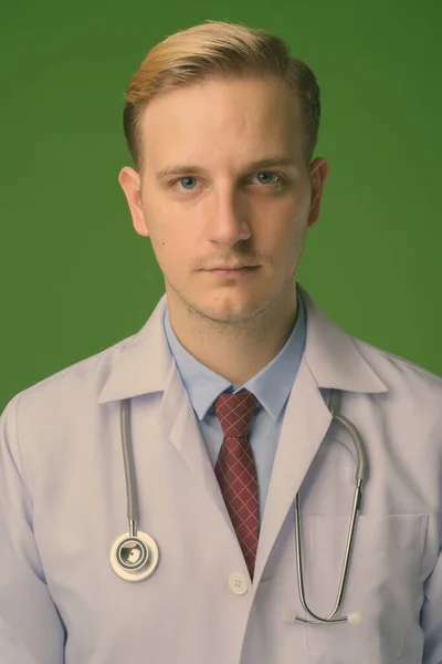Joven hombre guapo médico con el pelo rubio sobre fondo verde — Foto de Stock