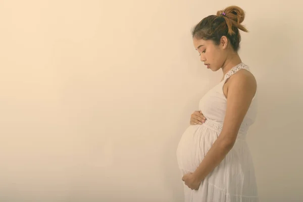 Beyaz arka planda karnını tutan Asyalı hamile kadının profil görüntüsü — Stok fotoğraf