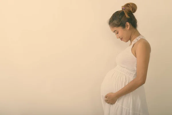 Vedere de profil a unei tinere asiatice gravide care se ține în timp ce se uită la stomac pe fundal alb — Fotografie, imagine de stoc