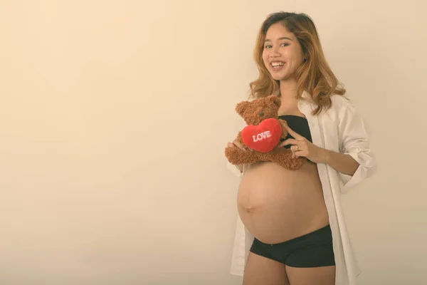 Studio strzał młody szczęśliwy Azji ciąży kobieta uśmiecha się trzymając misia z serca i znak miłości na białym tle — Zdjęcie stockowe