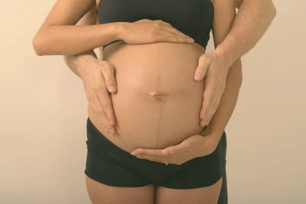 Estúdio tiro de mãos de jovem mulher grávida asiática com o homem segurando seu estômago juntos contra o fundo branco — Fotografia de Stock