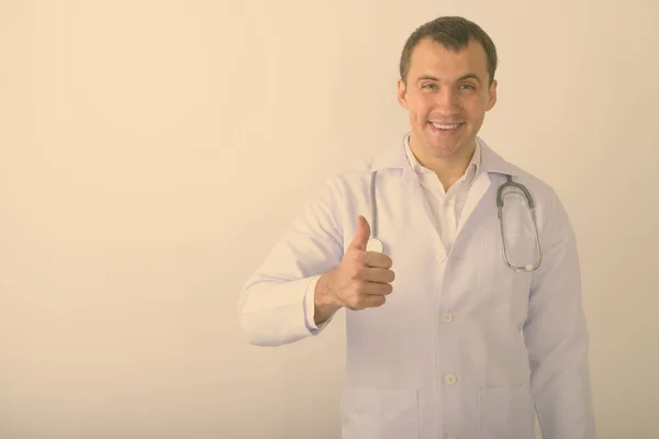 스튜디오에서는 하얀 배경에 엄지손가락을 대면서 웃고 있는 젊고 건강 한 근육질의 의사를 찍고 있다 — 스톡 사진