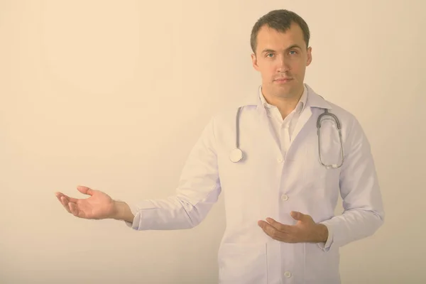 Estúdio tiro de jovem homem muscular médico mostrando algo contra fundo branco — Fotografia de Stock