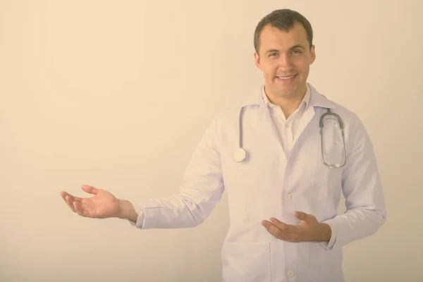 Estudio de tiro de joven feliz musculoso médico hombre sonriendo mientras muestra algo sobre fondo blanco —  Fotos de Stock