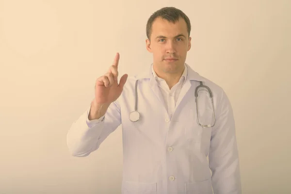 Estúdio tiro de jovem homem muscular médico apontando dedo para cima contra fundo branco — Fotografia de Stock