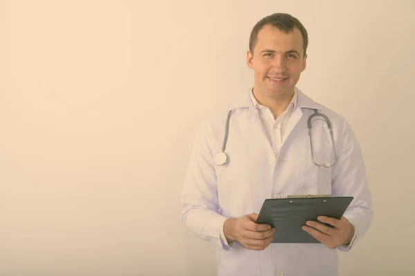 Студійний знімок молодого щасливого м'язистого лікаря, який посміхається, тримаючи кишеню на білому тлі — стокове фото
