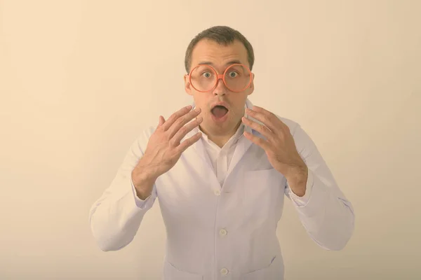 Студійний знімок молодого м'язистого лікаря, який виглядає здивованим під час носіння окулярів на білому тлі — стокове фото