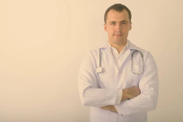 Estúdio tiro de jovem homem muscular médico com braços cruzados contra fundo branco Fotografia De Stock