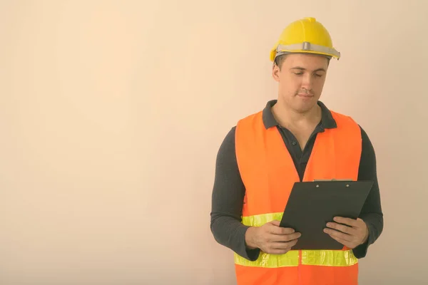 Studio shot of young muscular man construction worker reading on clipboard against white background — Stock Photo, Image