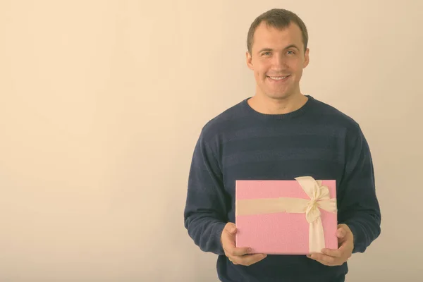 Studio shot van jonge gelukkig gespierde man glimlachen terwijl het houden van geschenkdoos tegen witte achtergrond — Stockfoto