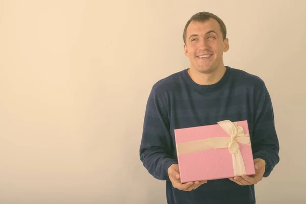 Studio shot van jonge gelukkig gespierde man glimlachen en denken terwijl het houden van geschenkdoos tegen een witte achtergrond — Stockfoto