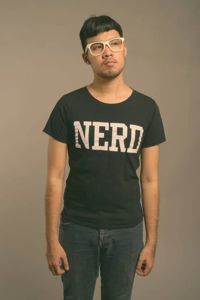 Joven asiática nerd hombre usando anteojos contra gris fondo — Foto de Stock