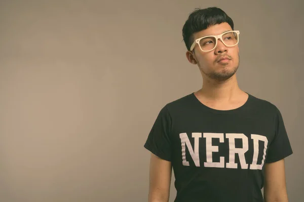 Joven asiática nerd hombre usando anteojos contra gris fondo —  Fotos de Stock