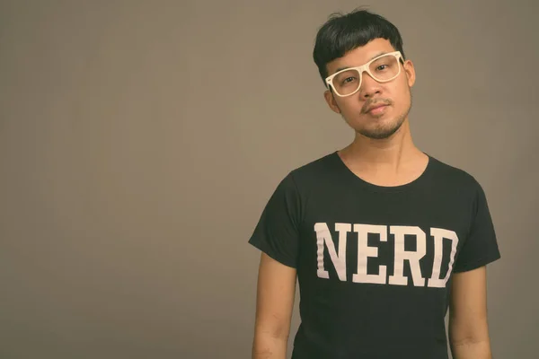 Joven asiática nerd hombre usando anteojos contra gris fondo —  Fotos de Stock