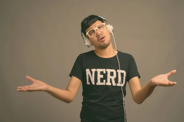 Joven asiática nerd hombre escuchar música contra gris fondo —  Fotos de Stock