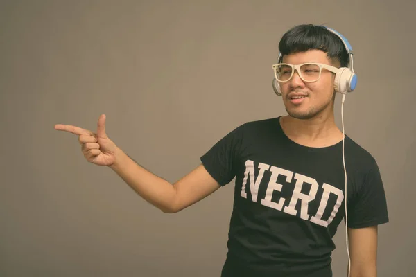 Junger asiatischer Nerd hört Musik vor grauem Hintergrund — Stockfoto
