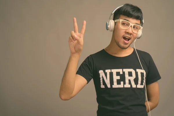 Junger asiatischer Nerd hört Musik vor grauem Hintergrund — Stockfoto