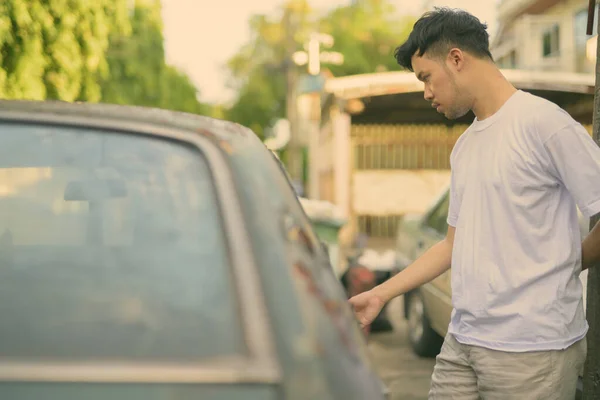 Молодий азіат з іржавою старою машиною на вулиці. — стокове фото