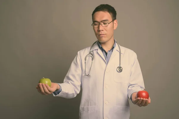 Joven asiático hombre médico contra gris fondo —  Fotos de Stock