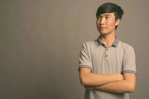 Mladý asijský muž na sobě šedé polo košile proti šedému pozadí — Stock fotografie