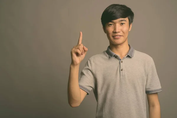 Mladý asijský muž na sobě šedé polo košile proti šedému pozadí — Stock fotografie