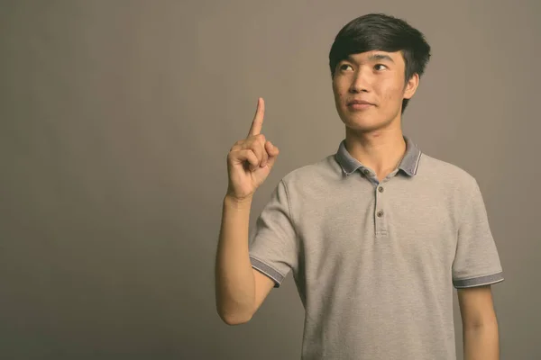 Fiatal ázsiai férfi szürke pólót visel szürke háttér — Stock Fotó