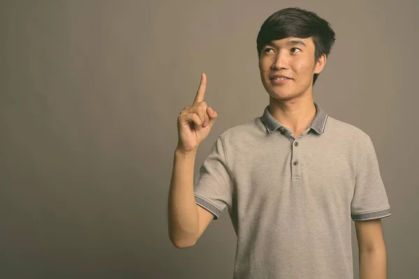 Ung asiatisk man bär grå pikétröja mot grå bakgrund — Stockfoto