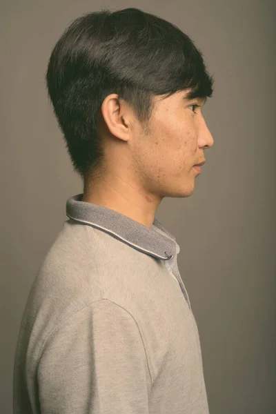 Gri arka planda gri polo tişört giyen genç Asyalı adam. — Stok fotoğraf